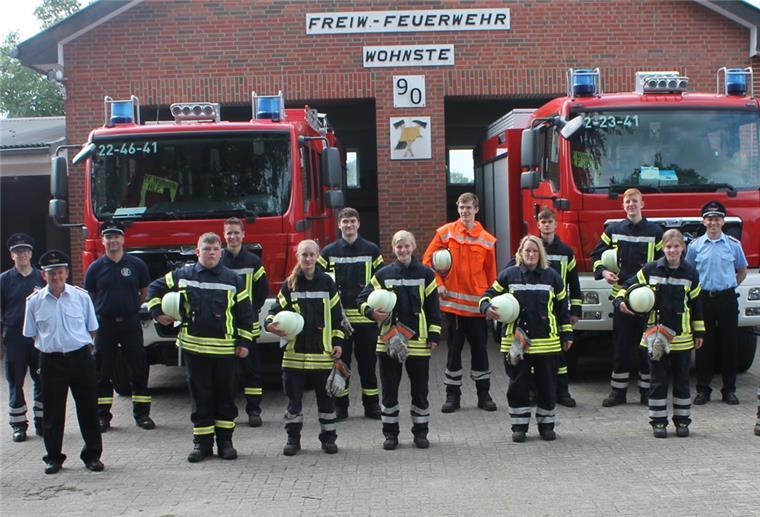 Junge Feuerwehrleute vor zwei Feuerwehrfahrzeugen