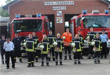 Junge Feuerwehrleute vor zwei Feuerwehrfahrzeugen