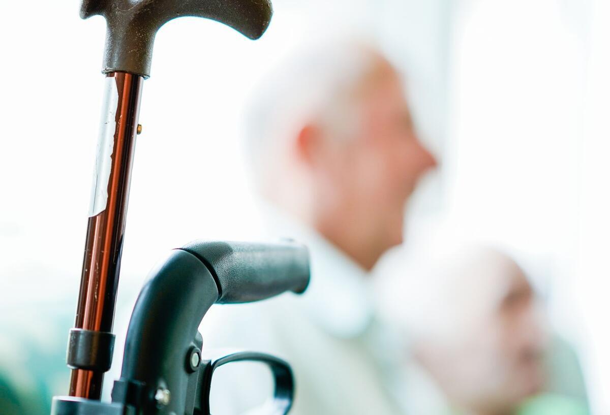 Revolutionäre Idee oder notwendiger Schritt? Pflichtarbeit für Senioren Der Teil eines Rollators und eines Gehstocks. In Hintergrund sieht man unscharf einen Rentner.