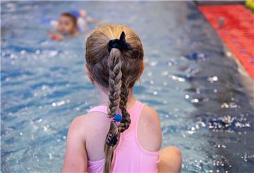 Ein Mädchen sitzt am Beckenrand eines Schwimmbades.
