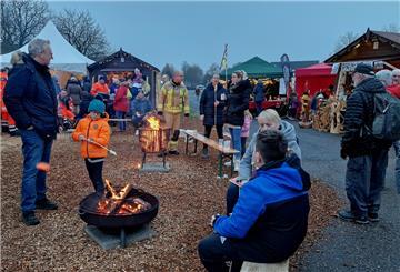 Menschen sitzen und stehen an Feuerschalen und Feuerkörben.