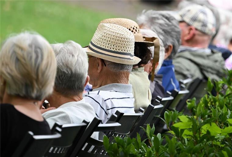 Ältere Menschen besuchen in einem Kurpark das Konzert eines Schulorchesters. 