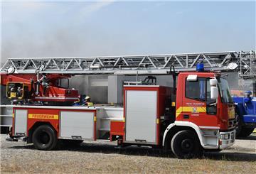 Ein Feuerwehrfahrzeug mit Drehleiter steht auf dem Parkplatz eines in Brand geratenen Autohauses