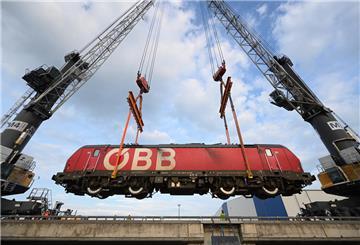 Eine E-Lok von Rail Cargo Carrier Germany (RCC) wird mit zwei Kränen auf das Binnenschiff „Rolf-Hein" gehoben und auf dem Seeweg nach Bremen transportiert.