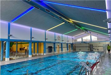 Ein Sportschwimmbecken mit einer neuen grauen Schallschutzdecke und blauen, gelben und grünen Leuchtstoffröhren.