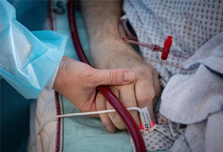 Eine Krankenschwester versorgt einen schwer an Corona erkrankten Patienten auf der Intensivstation des Klinikums in Fulda und hält dabei die Hand des Mannes. 