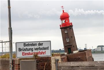 Der kleine Leuchtturm steht in Schieflage, davor steht ein Schild mit der Aufschrift: Betreten der Brüstung verboten! Einsturzgefahr!