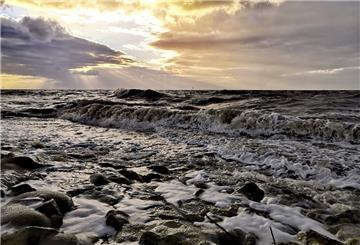 Die tobende Nordsee. Darüber brechen Sonnenstrahlen durch die grauen Wolken.