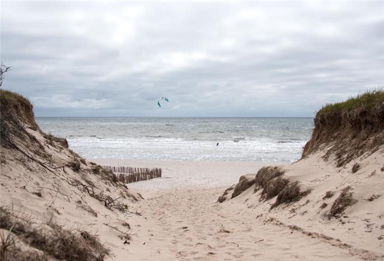 Ein Kitesurfer ist auf der Nordseeinsel am Strand von Rantum auf der Nordsee unterwegs, über der dunkle Wolken hängen.