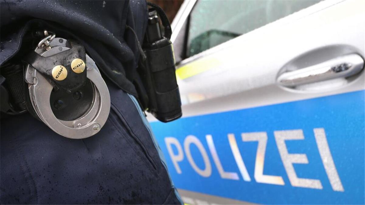 Raub in Lehe: Pärchen mit Schlägen und Tritten attackiert Ein Polizist mit Handschellen und einer Pistole am Gürtel steht vor einem Streifenwagen.