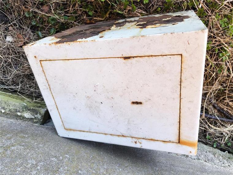 Ein weißer Tresor liegt auf einem asphaltierten Weg. Rostige Stellen sind zu sehen. 
