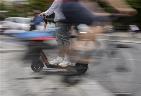 Ein Mann kreuzt mit einem E-Tretroller einen Fahrradfahrer. 