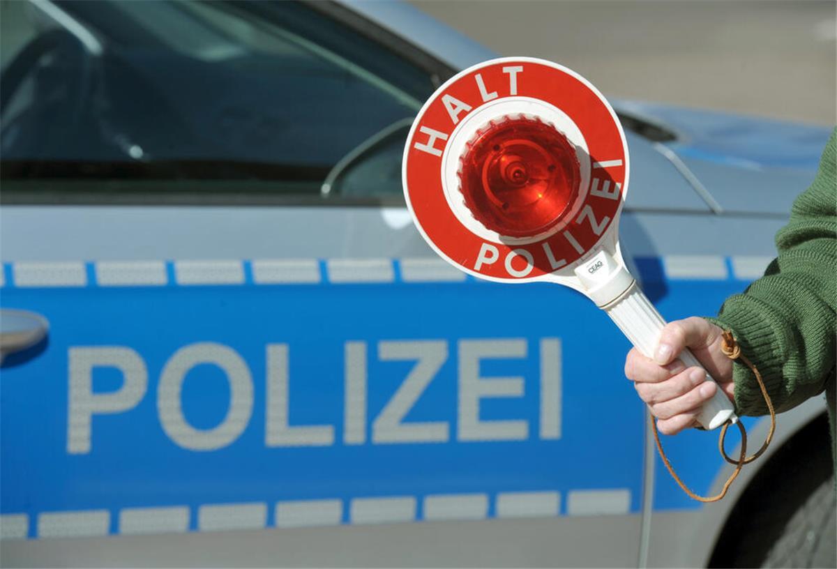 Eine Haltekelle wird von einem Polizisten vor einem Polizeifahrzeug.