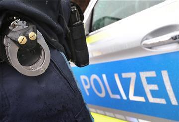 Ein Polizist mit Handschellen und einer Pistole am Gürtel steht vor einem Streifenwagen. 
