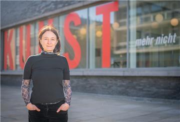 Stefanie Kleefeld steht vor einem Gebäude mit der roten Aufschrift Kunst