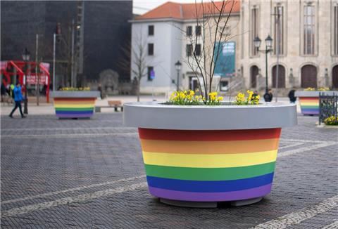 Ein Kübel in regenbogenfarben ist auf einem öffentlichen Platz zu sehen.