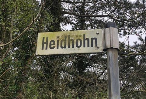 Ein Straßenschild mit der Beschriftung "Heidhöhn" vor einigen Bäumen