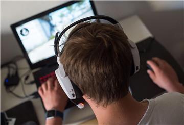 Ein junger Mann sitzt mit einem Headset vor einem Laptop und spielt ein Online-Computerspiel