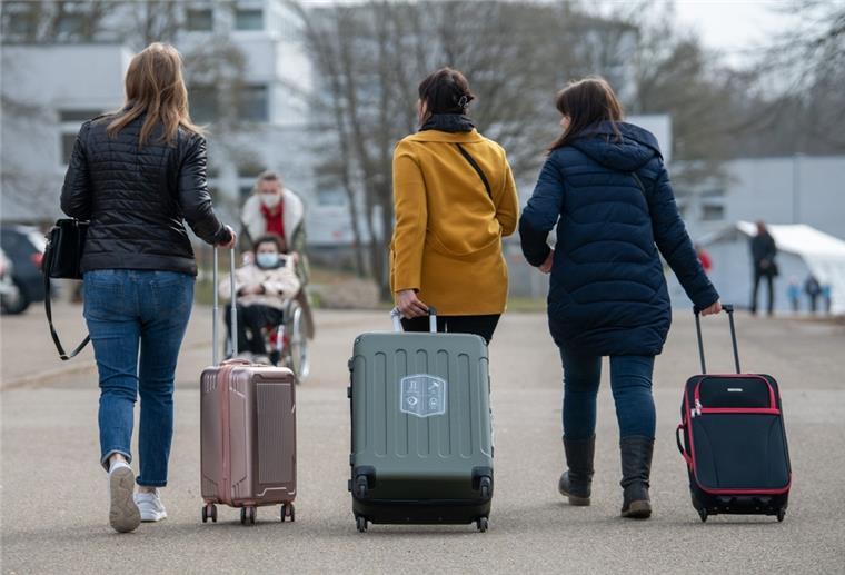 Drei Frauen ziehen drei Rollkoffer. Im Hintergrund wird eine Person im Rollstuhl geschoben.