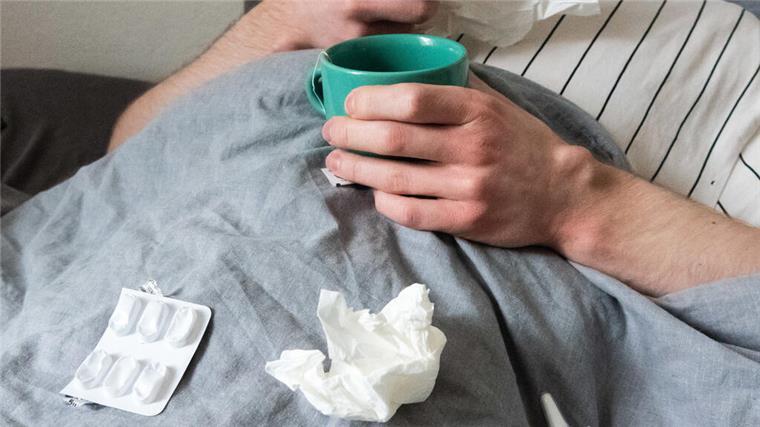  Ein Mann liegt mit Taschentüchern, Teetasse, Nasenspray und Tabletten im Bett (gestellte Szene). 