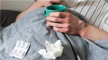  Ein Mann liegt mit Taschentüchern, Teetasse, Nasenspray und Tabletten im Bett (gestellte Szene). 