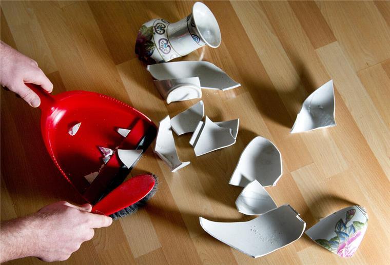 Das zahlt deine Haftpflichtversicherung und das nicht! Ein Mann kehrt eine kaputte Vase mit einem Handfeger auf.