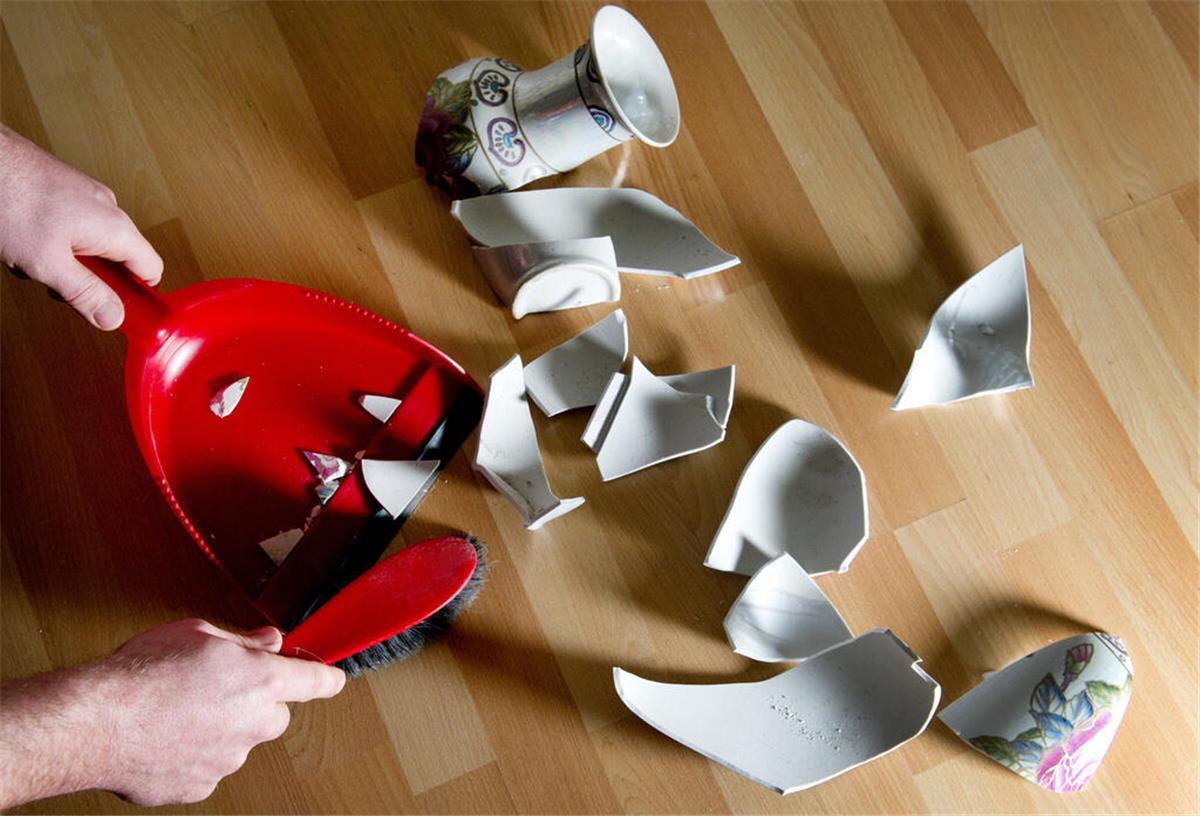 Ein Mann kehrt eine kaputte Vase mit einem Handfeger auf.