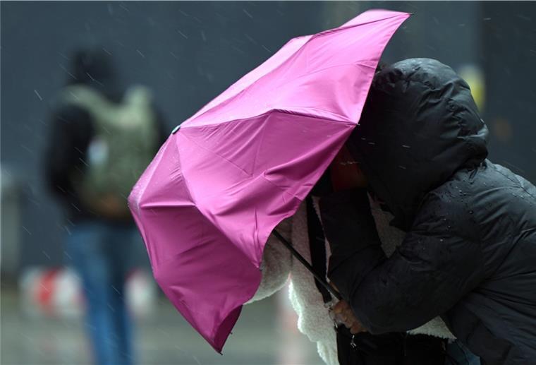 Passanten kämpfen mit dem Wind und ihrem Regenschirm. 