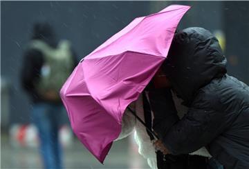 Passanten kämpfen mit dem Wind und ihrem Regenschirm. 