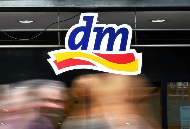 Eine DM-Filiale und das Markenlogo. Im Vordergrund unscharfe Menschen.