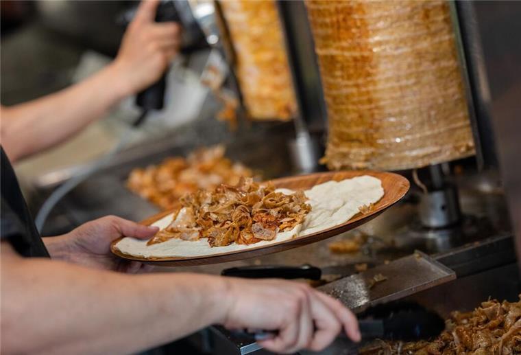 Preise bald über 10 Euro? Warum Döner jetzt deutlich teurer werden Ein Mitarbeiter einer Dönerbude legt Fleisch auf einen Döner.