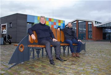 Dr. Ralf Meyer (Erlebnis Bremerhaven, links) und Sebastian Gregorius (Fischereihafen-Betriebsgesellschaft) machen es sich auf der neuen „Fischbank“ im Schaufenster Fischereihafen gemütlich.