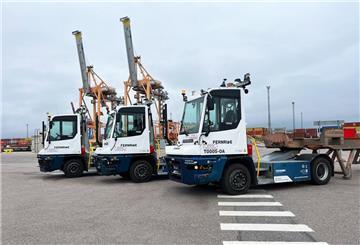 Drei autonome Terminal-Zugmaschinen von FERNRIDE stehen nebeneinander auf einem Containerterminal, im Hintergrund Container und Hafenkräne.