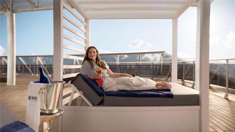 Kreuzfahrtschiff „MSC World America“: Dieser Weltstar übernimmt erstmals die Taufe Eine Frau liegt auf einer schicken Liege auf einem Kreuzfahrtschiff, lächelt und hält ein Glas in der Hand. Die US-Schauspielerin Drew Barrymore tauft das neue Kreuzfahrtschiff "MSC World America".
