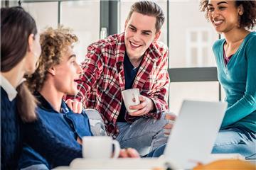 Gruppe lachender Studenten trinkt gemeinsam Kaffee.