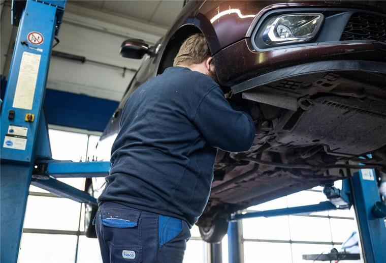 Kfz-Versicherung: Werkstattbindung und Selbstbeteiligung sparen hunderte Euro! Ein Mechaniker schaut in den Radkasten eines Autos einer Kfz-Werkstatt.