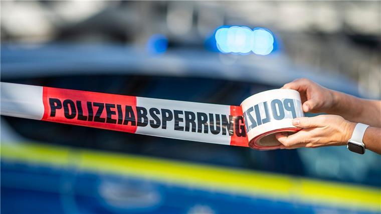 Ein Absperrband wird vor einem Polizeiwagen ausgerollt.