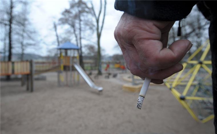 Ein Mann hält auf einem Spielplatz eine Zigarette in der Hand.