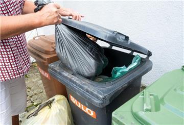 Eine Frau wirft einen Sack mit Restmüll in eine graue Restmülltonne.