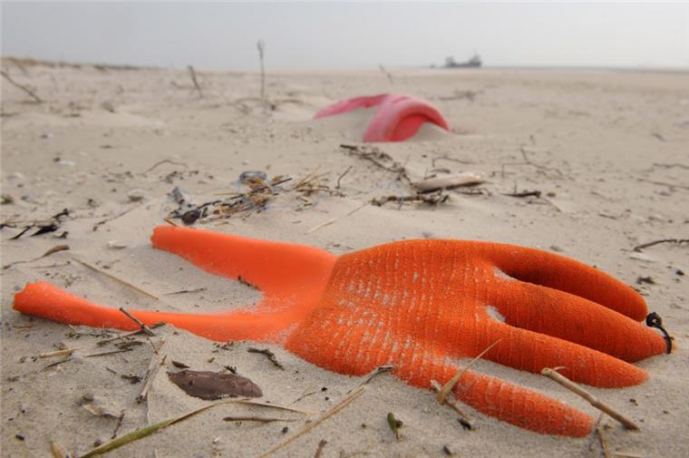 Ein angespülter Arbeitshandschuh und ein Kunststoffkanister am Strand 
