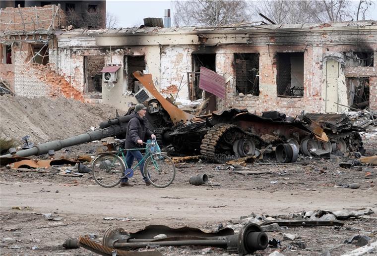 Ein Anwohner geht mit seinem Fahrrad vor beschädigten Gebäuden und einem Panzer vorbei, etwa 400 km östlich der Hauptstadt Kiew.