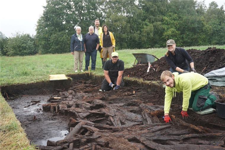 Ein Archäologenteam legt einen Streckenabschnitt des historischen Moorwegs frei. Im Hintergrund beobachten Dr. Stefan Hesse (hinten) und Dr. Marion Heumüller (rechts), Fachbereichsleiterin im Landesamt für Denkmalpflege, gemeinsam mit dem Ehepaar Specht die Arbeiten von Lennart Picht (rechts), Ingo Neumann und Jetta Harms.