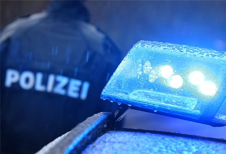 Lehe: Mann (29) randaliert in Treppenhaus Ein Polizist steht im Regen vor einem Streifenwagen dessen Blaulicht aktiviert ist.