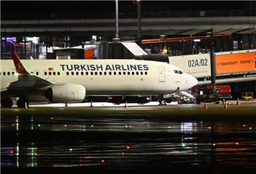 Ein Polizeifahrzeug steht auf dem Flughafen vor einem Flugzeug, an dem ein Auto mit einem Geiselnehmer steht.