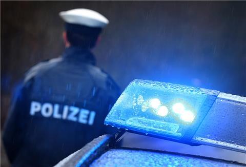 Ein Polizist steht im Regen vor einem Streifenwagen dessen Blaulicht aktiviert ist