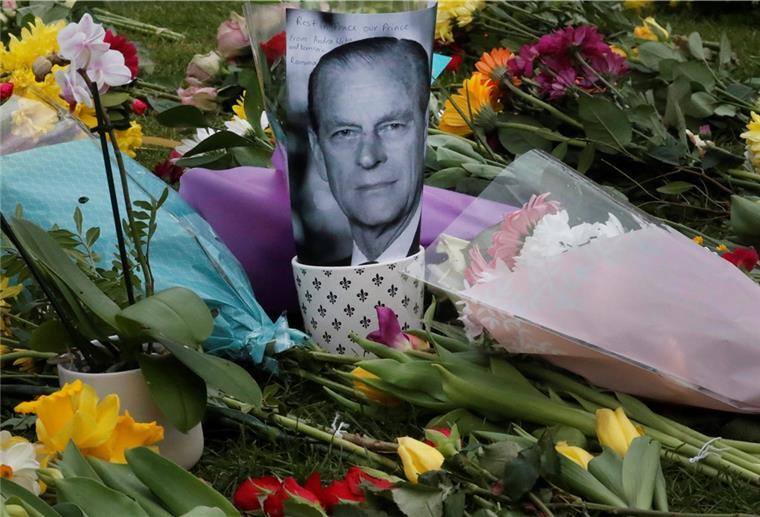 Ein Bild des verstorbenen Prinz Philip ist neben Blumen am Schloss Windsor abgelegt. Wegen der Corona-Pandemie soll bei der Trauerzeremonie auf öffentliche Prozessionen verzichtet werden.