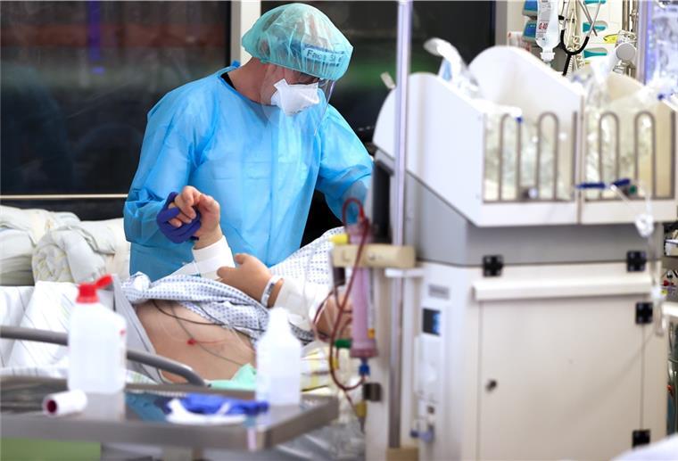 Immer mehr Corona-Patienten werden verlegt Ein Facharzt versorgt einen Covid-19-Patienten auf der Intensivstation der Leipziger Uniklinik und hält dessen Hand.