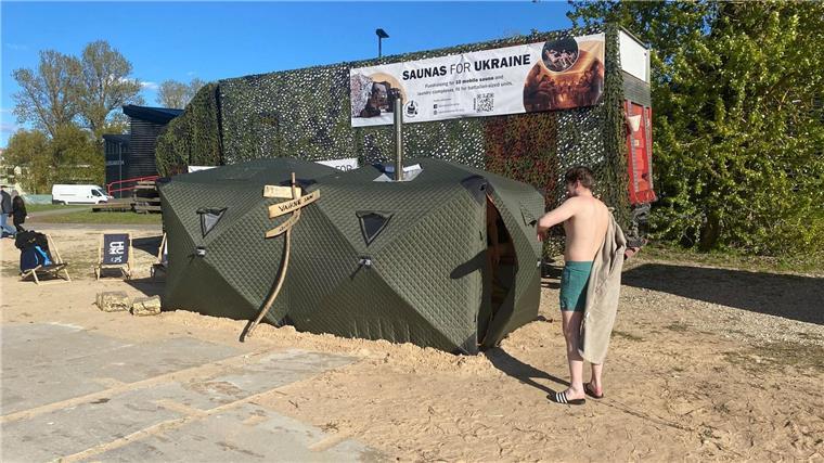 Ein Festival-Besucher steht vor einer mobilen Front-Sauna, die in Estland für die ukrainische Armee entwickelt worden ist.