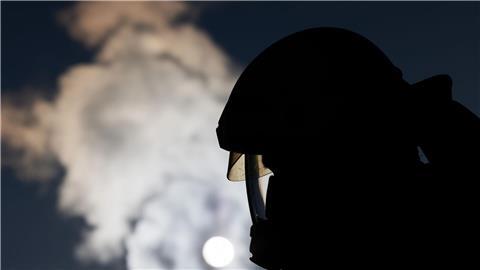 Ein Feuerwehrmann in Atemschutzausrüstung steht an einem Einsatzfahrzeug.