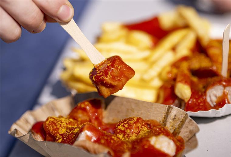 Ein Genussmoment im Zeichen der Tradition – eine Person genießt eine Currywurst zum 75. Jahrestag ihrer Erfindung. Ein kulinarisches Kulturerbe, das deutschlandweit begeistert.